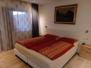 a bedroom with a bed with a red comforter and a window at kuglerhof in Dobbiaco