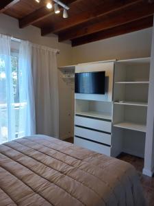 1 dormitorio con 1 cama, TV y estanterías en Acacia Morada, en Villa Gesell