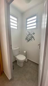 a white bathroom with a toilet and two windows at Appartement vue mer Chez Ti Louis - Grande Anse in Les Anses-dʼArlets
