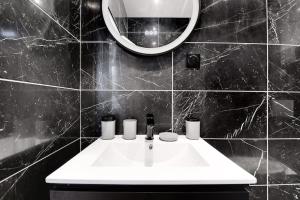 Baño de azulejos negros con lavabo y espejo en Appartement aux Portes de Paris en Saint-Denis