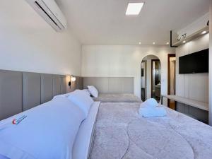 1 dormitorio con 2 camas con sábanas blancas y TV en Apartamentos Rossa Residenzialle CENTRO by Achei Gramado, en Canela