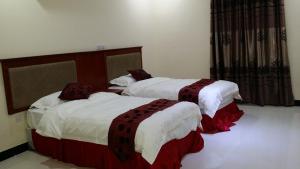 a bedroom with two beds with white and red sheets at Hana Yanbu Hotel Apartments in Yanbu