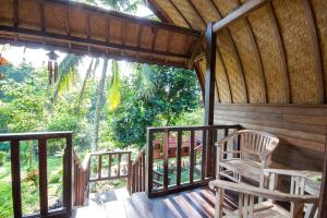 une terrasse couverte d'une cabane en bois avec un fauteuil à bascule dans l'établissement Bali Sesandan Garden, à Tabanan