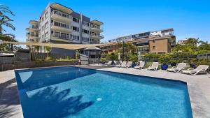 einen Pool mit Stühlen und ein Gebäude in der Unterkunft Cheltenham Apartments Unit 6 Kings Beach QLD in Caloundra