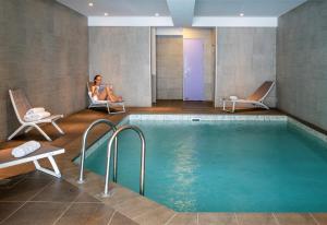 una camera d'albergo con piscina e due persone sedute sulle sedie di Hôtel L'Aiguille Percée a Tignes