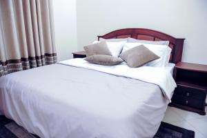 a bed with white sheets and pillows in a bedroom at Eric Wilkins Apartments in Kampala