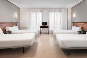 um quarto de hotel com camas brancas e uma televisão em Hotel Victoria Valdemoro em Valdemoro