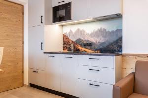 a kitchen with white cabinets and a painting on the wall at Planerhof Apartment Alpenrose in Funes
