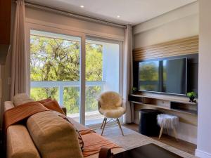 uma sala de estar com um sofá e uma grande janela em Apartamentos Delle Alpi by Achei Gramado em Canela