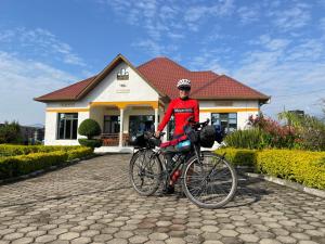 um homem parado ao lado de uma bicicleta em frente a uma casa em Virunga Homestays em Ruhengeri