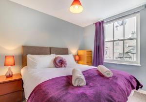 a bedroom with a large bed with purple sheets and a window at Greyhound Cottage in Kendal