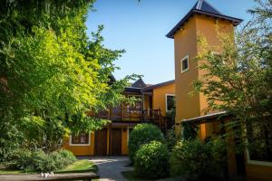 a large yellow house with a balcony and trees at Kau Kaleshen in El Calafate