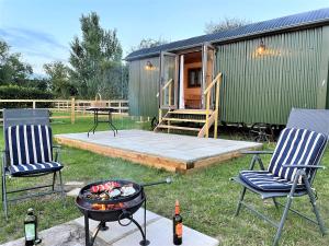 a backyard with two chairs and a grill and a house at The Huddle at Big Sky Brisley in Brisley