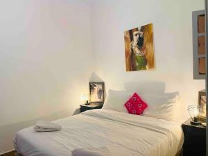 ein Schlafzimmer mit einem weißen Bett mit einem roten Kissen in der Unterkunft Jolie petit Riyad avec piscine belle terrasse wifi in Marrakesch