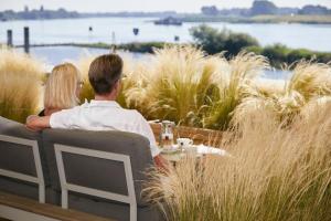 Ein Mann und eine Frau sitzen an einem Tisch mit Blick auf das Wasser in der Unterkunft Traditionshaus by Zollenspieker Fährhaus in Hamburg