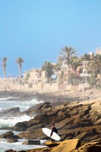 a man standing on a rocky beach holding a surfboard at Onda Surf in Taghazout