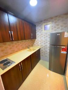 La cuisine est équipée d'un réfrigérateur en acier inoxydable et de placards en bois. dans l'établissement دريم العليا للوحدات السكنية, à Khobar