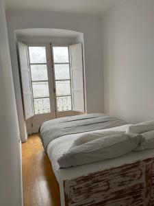 a white bedroom with a bed and two windows at GALLE - Apartamento dos Infantes in Beja