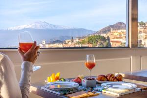 una persona che tiene in mano un bicchiere di vino davanti a un tavolo con cibo di Hotel Villa Paradiso a Taormina