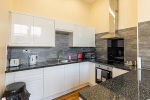 uma cozinha com armários brancos e bancadas pretas em New 2 bed apartment with stunning views of Arthur Seat Mountain em Edimburgo