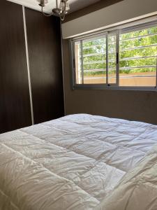 1 cama blanca en un dormitorio con ventana en Depto Chascomus en Chascomús