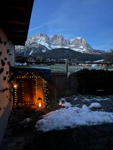 a house with a lit up door with snowy mountains in the background at Mona Apartment in Going am Wilden Kaiser