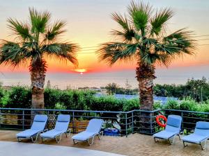 a group of chairs and palm trees on a patio with a sunset at Oasis Scaleta Hotel in Skaleta