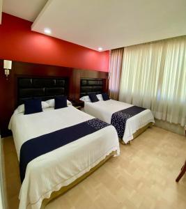 2 letti in una camera d'albergo con pareti rosse di HOTEL IMPALA DE TAMPICO a Tampico