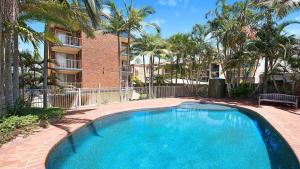 a swimming pool in front of a building with palm trees at Kookaburra Court Unit 1 Bulcock Beach QLD in Caloundra