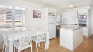 een keuken met witte kasten en een witte tafel en stoelen bij Kookaburra Court Unit 3 Bulcock Beach QLD in Caloundra