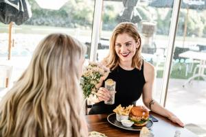 a woman sitting at a table with a hamburger and fries at Tides Hotel in Nelson