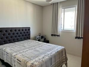 a bedroom with a bed with a blanket and a window at apartamento praia do morro - beira mar in Guarapari