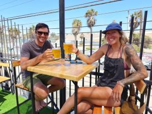 un hombre y una mujer sentados en una mesa con vasos de cerveza en Hostel Willka Kuti Backpackers en Arica
