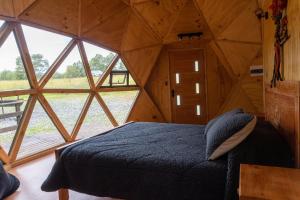 Cama en habitación con ventana grande en Domos Ngen Mawida de Licanray, en Licán Ray