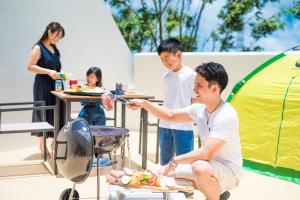沖縄市にあるライカムファミリーリゾートホテル旧HiyagunLanaiResortのテントの前の焼き物の周りに立つ人々