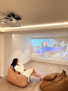 a woman sitting on a couch in a room with a car on the wall at 婧仕女微旅 in Hou-lung-tzu
