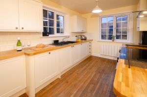 a kitchen with white cabinets and wooden floors and windows at Thrang Close, Chapel Stile in Chapel Stile