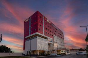 Ramada Encore by Wyndham Guadalajara Aeropuerto في غواذالاخارا: مبنى فندق أحمر طويل مع سماء غائمة