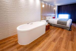 a bathroom with a bath tub in front of a bed at Ramada Encore by Wyndham Guadalajara Aeropuerto in Guadalajara