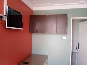a kitchen with brown cabinets and a tv on the wall at Bethel Resort & Hotels in Gulu