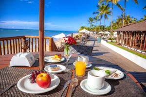 uma mesa com comida e bebidas numa varanda com o oceano em Saint Tropez Praia Hotel em Arraial d'Ajuda