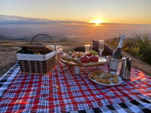 a picnic blanket with a table with food and a sunset at Morada Alto Das Nuvens in São José dos Ausentes
