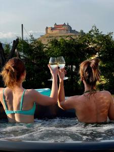 Domček pod orechom في Krásnohorské Podhradie: اثنتان من النساء يجلسن في الماء يحملن كؤوس النبيذ