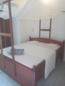 1 dormitorio con cama de madera con sábanas blancas en Iddi House en Jambiani