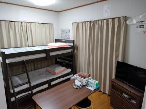 a room with bunk beds and a table and a television at Guesthouse Maple Nikko in Nikko