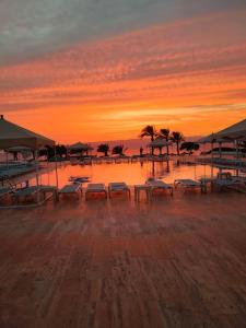 einen Sonnenuntergang über einem Strand mit Bänken und Bäumen in der Unterkunft Sun and beach apartment in Aqaba