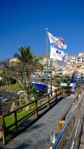 a boardwalk near a beach with a flag and buildings at La Arena sunflowers in Puerto de Santiago