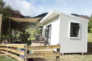 a small white tiny house with a wooden fence at Cable Bay Farm in Nelson