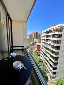 einen Tisch mit Tassen auf einem Balkon mit Blick auf ein Gebäude in der Unterkunft Lindo y equipado depto de 1d/1b en Metro Manquehue in Santiago