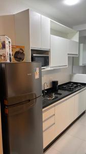 La cuisine est équipée d'un réfrigérateur en acier inoxydable et de placards blancs. dans l'établissement Apartamento Jardins Ubatuba, à Ubatuba